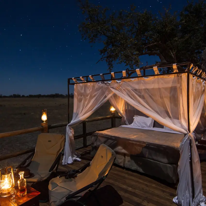Outdoor bedroom pavilion with curtains overlooking savanna at night, Kanana, The Okavango Delta, Botswana