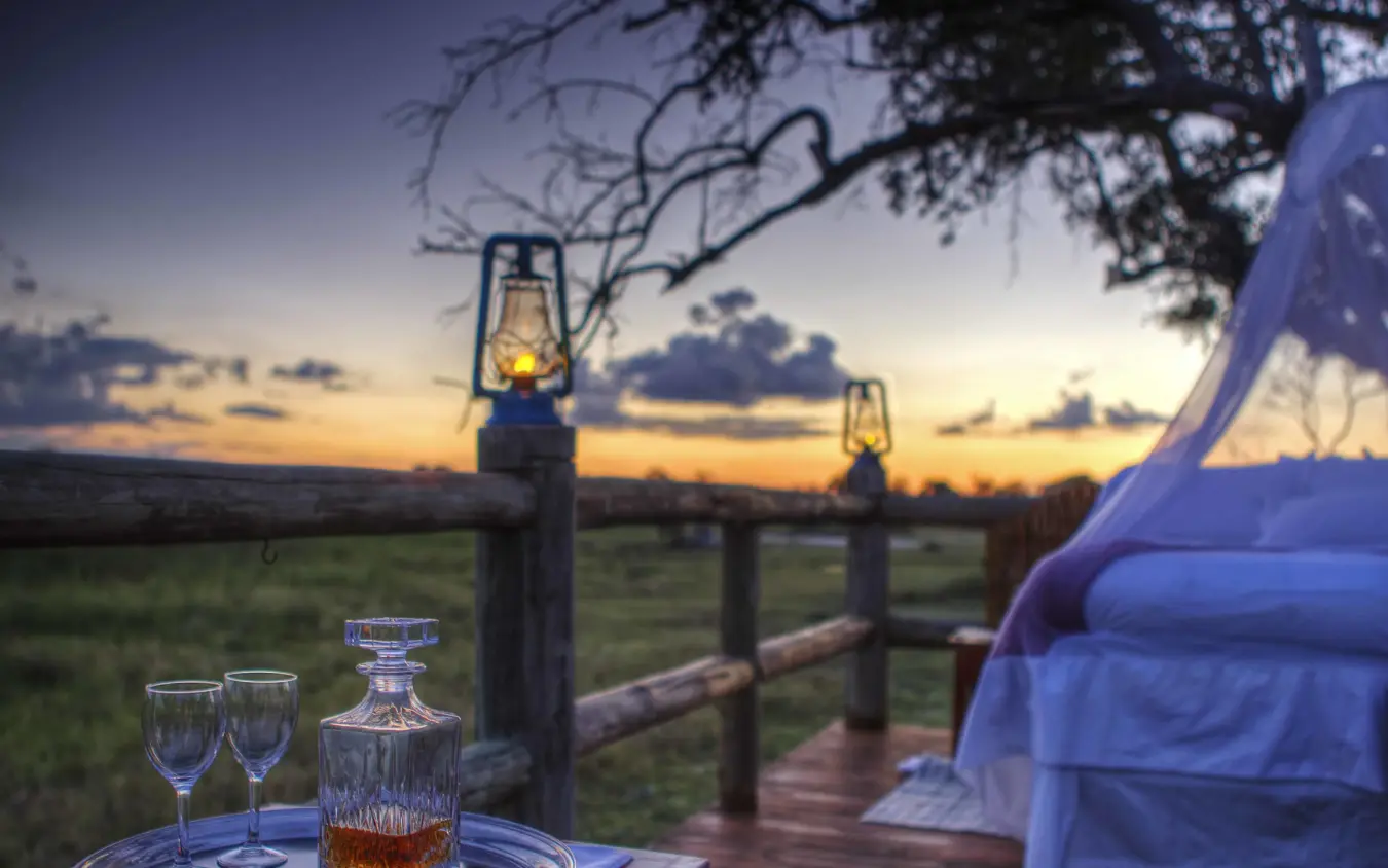 Wooden deck at sunset with glasses and decanter overlooking savanna, Kanana, The Okavango Delta, Botswana