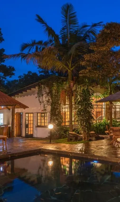 Illuminated lodge courtyard with infinity pool and mature trees at dusk, Karen Blixen Cottages, Nairobi, Kenya