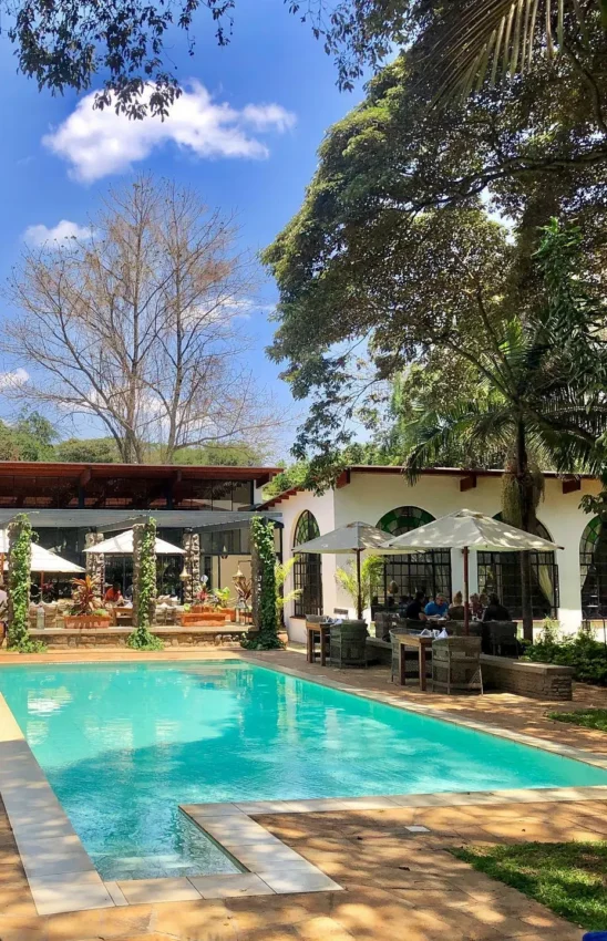 Luxury poolside lounge with white umbrellas and colonial architecture, Karen Blixen Cottages, Nairobi, Kenya