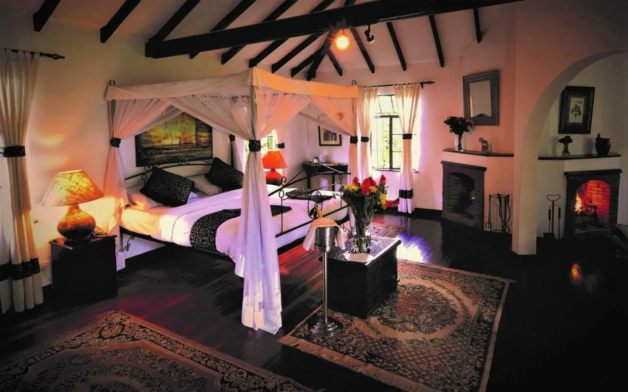 Luxury bedroom suite with four-poster bed and fireplace at night, Karen Blixen Cottages, Nairobi, Kenya