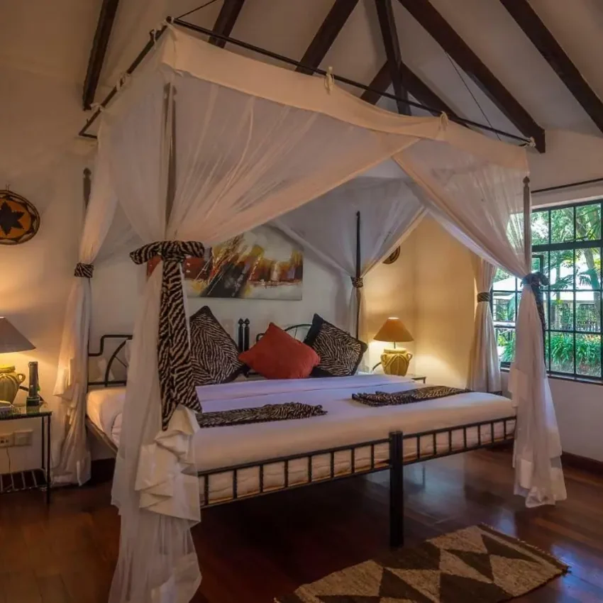 Four-poster bed with white drapes in colonial-style bedroom with exposed beams, Karen Blixen Cottages, Nairobi, Kenya