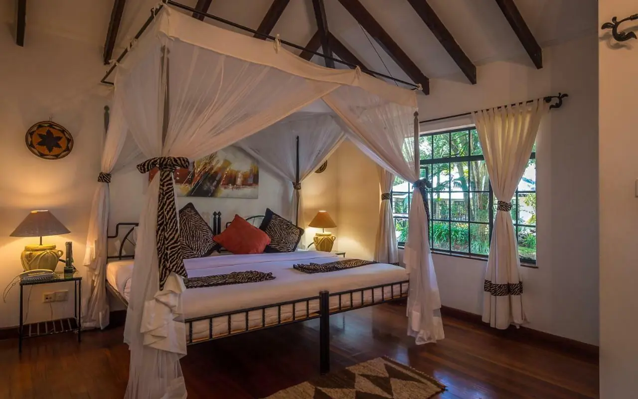 Four-poster bed with white drapes in colonial-style bedroom with exposed beams, Karen Blixen Cottages, Nairobi, Kenya