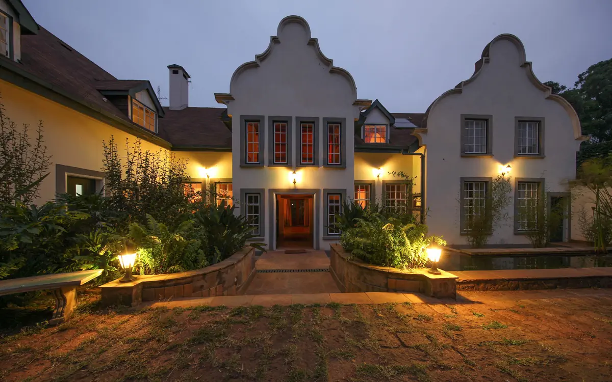 Whitewashed colonial lodge exterior illuminated at dusk with courtyard approach, Karen Gables, Nairobi, Kenya