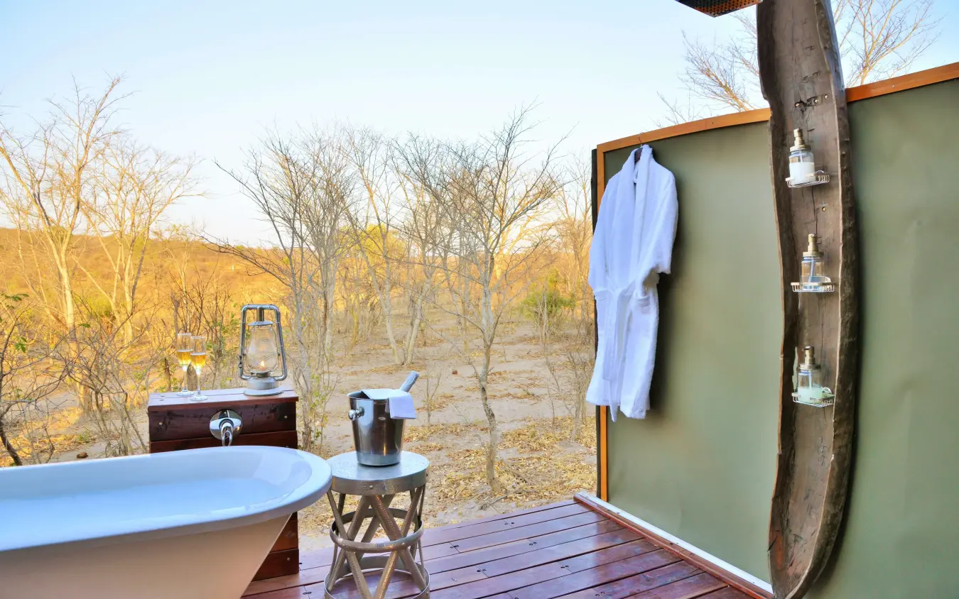 Outdoor bathtub on wooden deck with savanna views and bare trees, Khulu Bush Camp, Hwange National Park, Zimbabwe