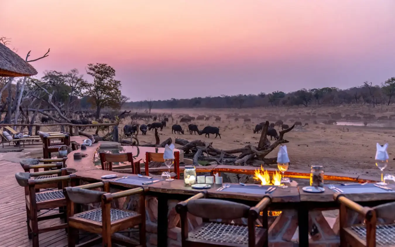 Outdoor dining deck with firepit overlooking elephants grazing at dusk, Khulu Bush Camp, Hwange National Park, Zimbabwe