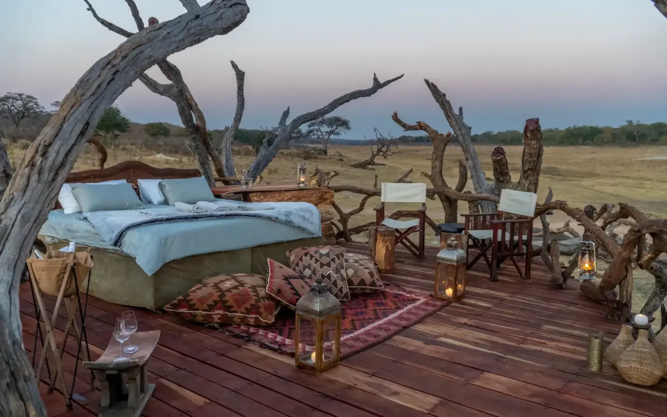 Open-air bedroom platform with dead trees overlooking grassland at dusk, Khulu Bush Camp, Hwange National Park, Zimbabwe
