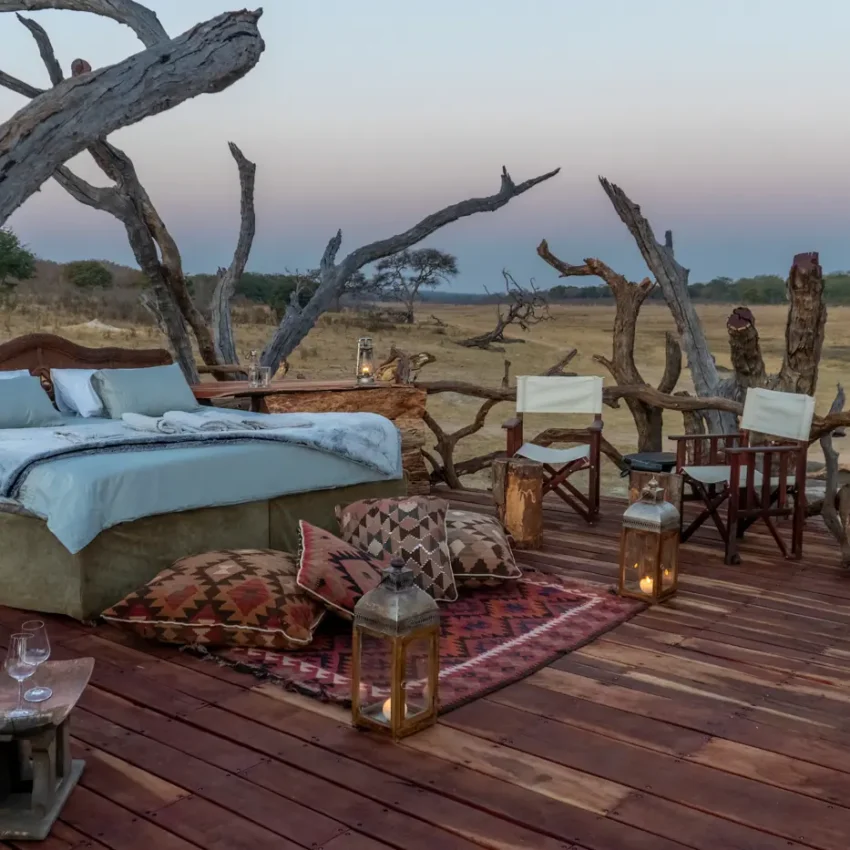 Open-air bedroom platform with dead trees overlooking grassland at dusk, Khulu Bush Camp, Hwange National Park, Zimbabwe