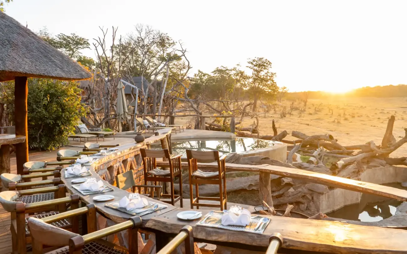 Outdoor dining area overlooking waterhole at sunset in arid savanna, Khulu Bush Camp, Hwange National Park, Zimbabwe