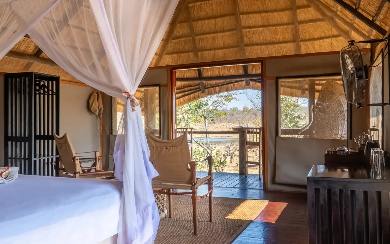 Luxury safari lodge bedroom with canopy bed overlooking savanna landscape, Khulu Bush Camp, Hwange National Park, Zimbabwe