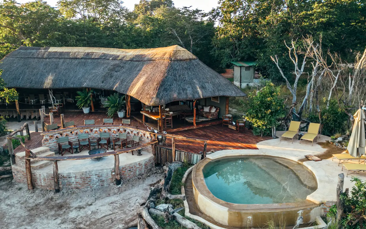Thatched lodge with thermal pools and outdoor lounge area surrounded by trees, Khulu Bush Camp, Hwange National Park, Zimbabwe