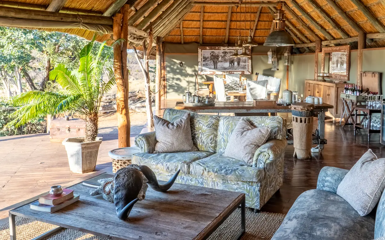 Open-air lodge lounge with blue patterned furniture and wooden beam ceiling, Khulu Bush Camp, Hwange National Park, Zimbabwe