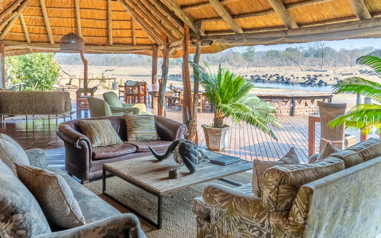 Thatched lounge overlooking river with elephants and wildlife at waterhole, Khulu Bush Camp, Hwange National Park, Zimbabwe