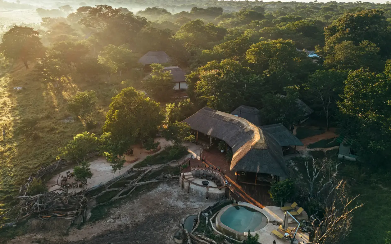 Aerial view of luxury lodge with curved roof structures nestled in dense forest canopy at sunrise, Khulu Bush Camp, Hwange National Park, Zimbabwe