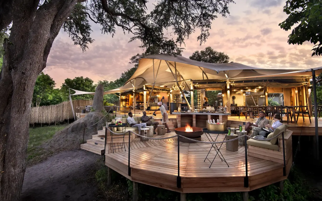 Illuminated safari lodge deck with fire pit at dusk, Khwai Leadwood, The Okavango Delta, Botswana