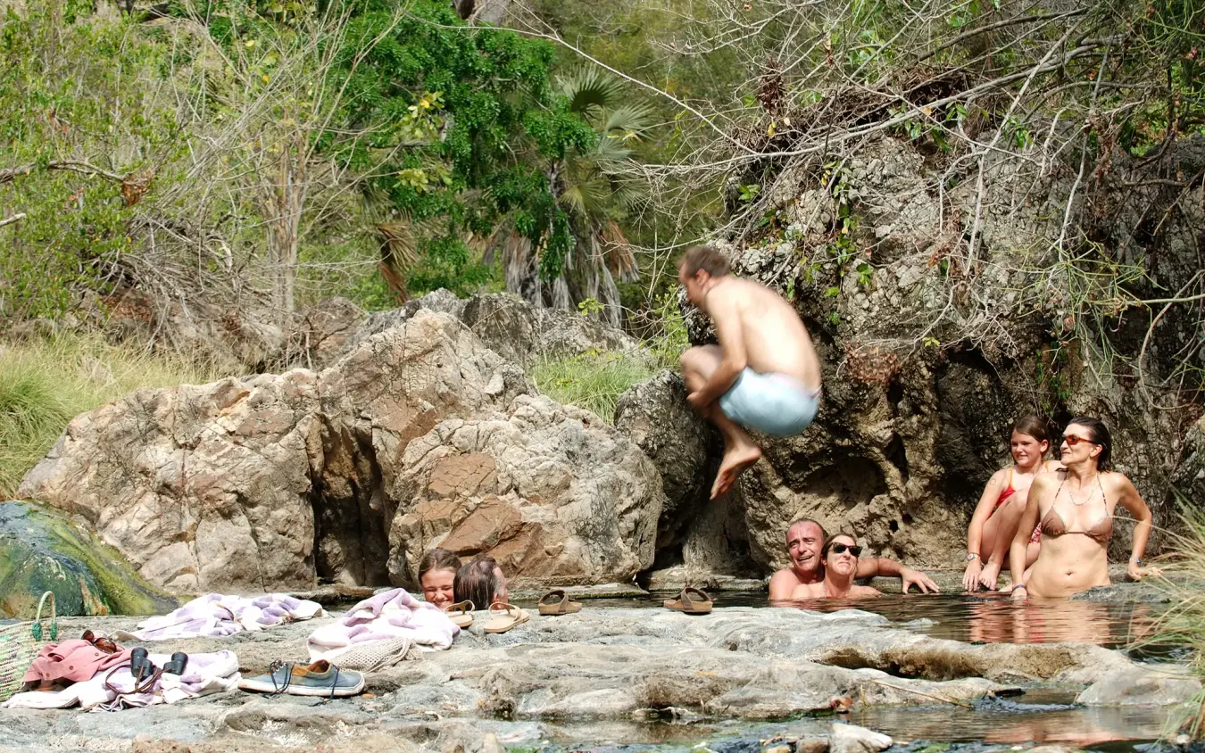 Group of people swimming and relaxing in natural rock pool with vegetation, Kiba Point, Nyerere National Park, Tanzania