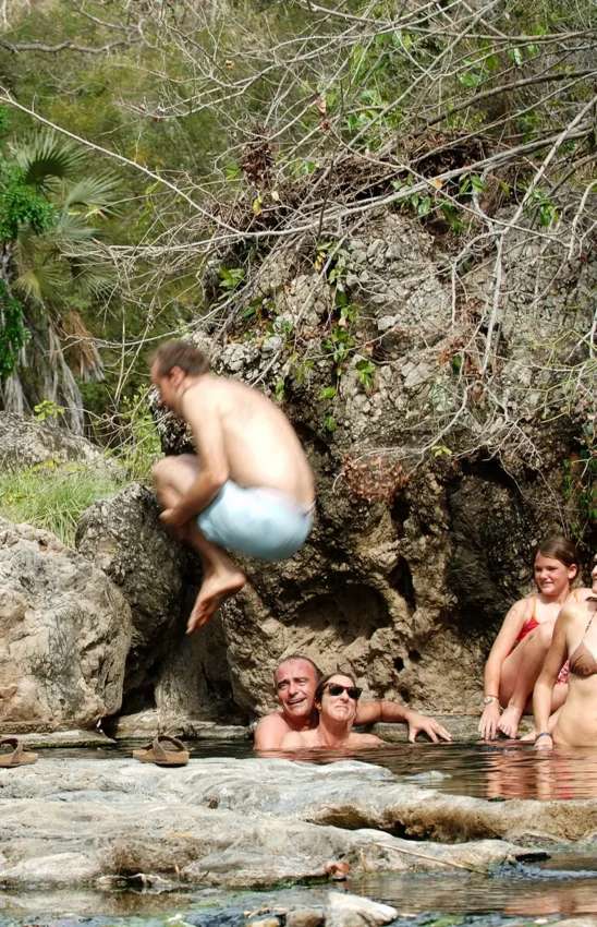 Group of people bathing in natural hot spring pool surrounded by rocks and vegetation, Kiba Point, Nyerere National Park, Tanzania