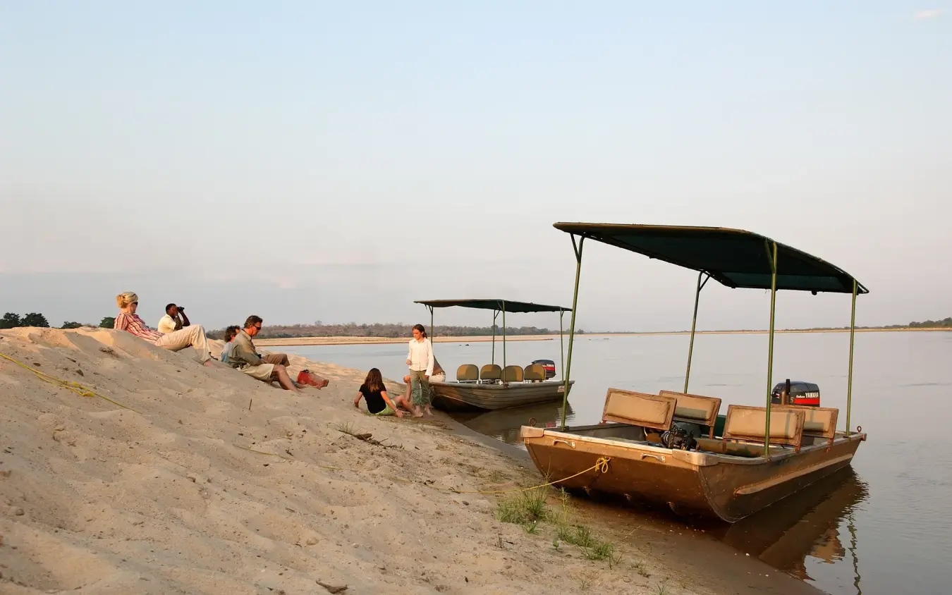 Wooden boats with black canopies moored on sandy riverbank at dusk, Kiba Point, Nyerere National Park, Tanzania