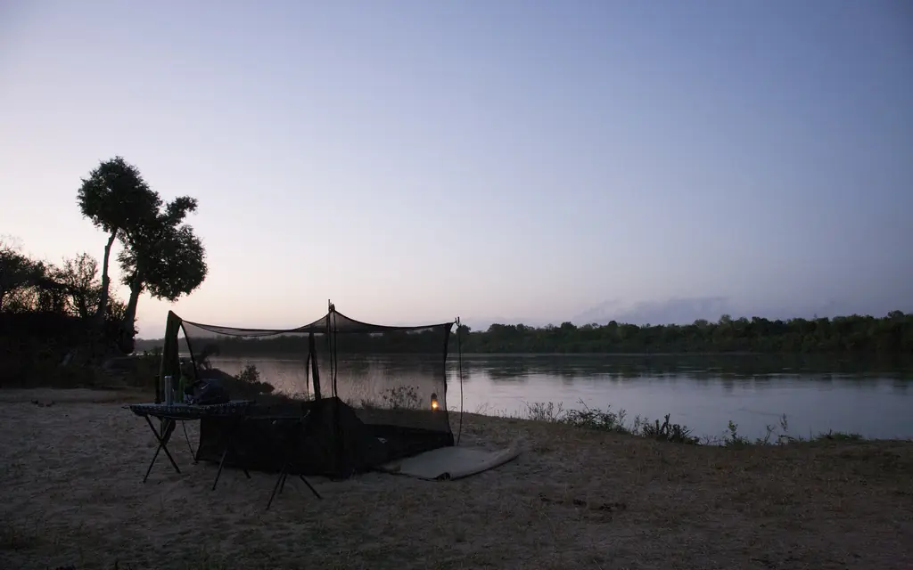 Riverside camp with mosquito net canopy at dusk overlooking river, Kiba Point, Nyerere National Park, Tanzania