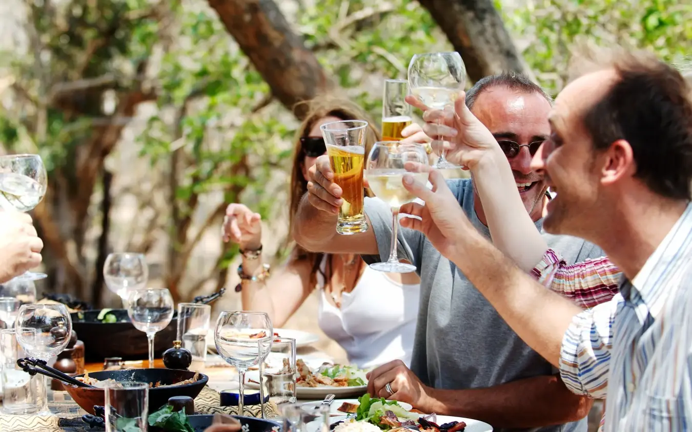 Group toasting with wine and beer at outdoor lunch table under tree, Kiba Point, Nyerere National Park, Tanzania