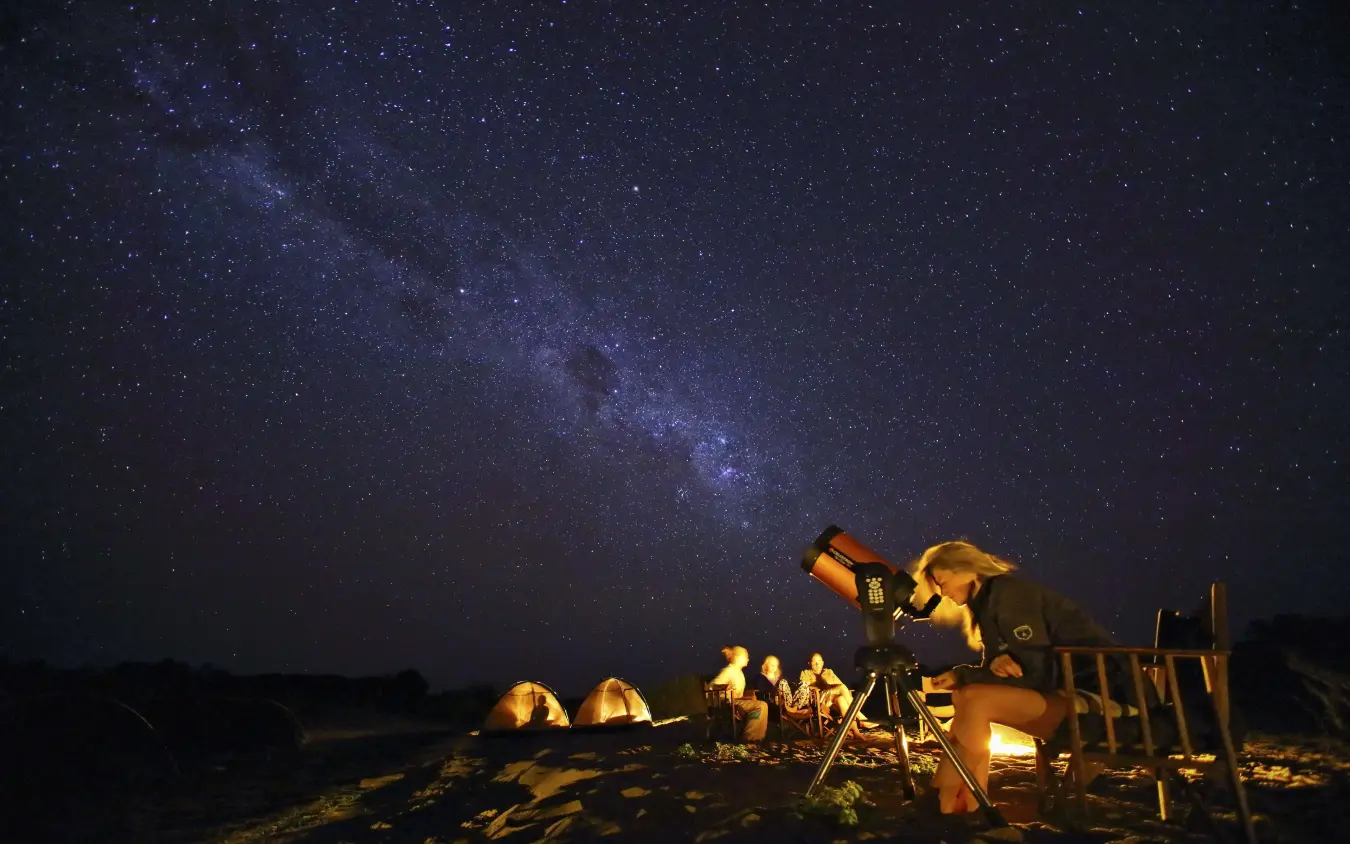 Guests stargazing at night with telescope under Milky Way, Kichaka Expeditions, Ruaha National Park, Tanzania