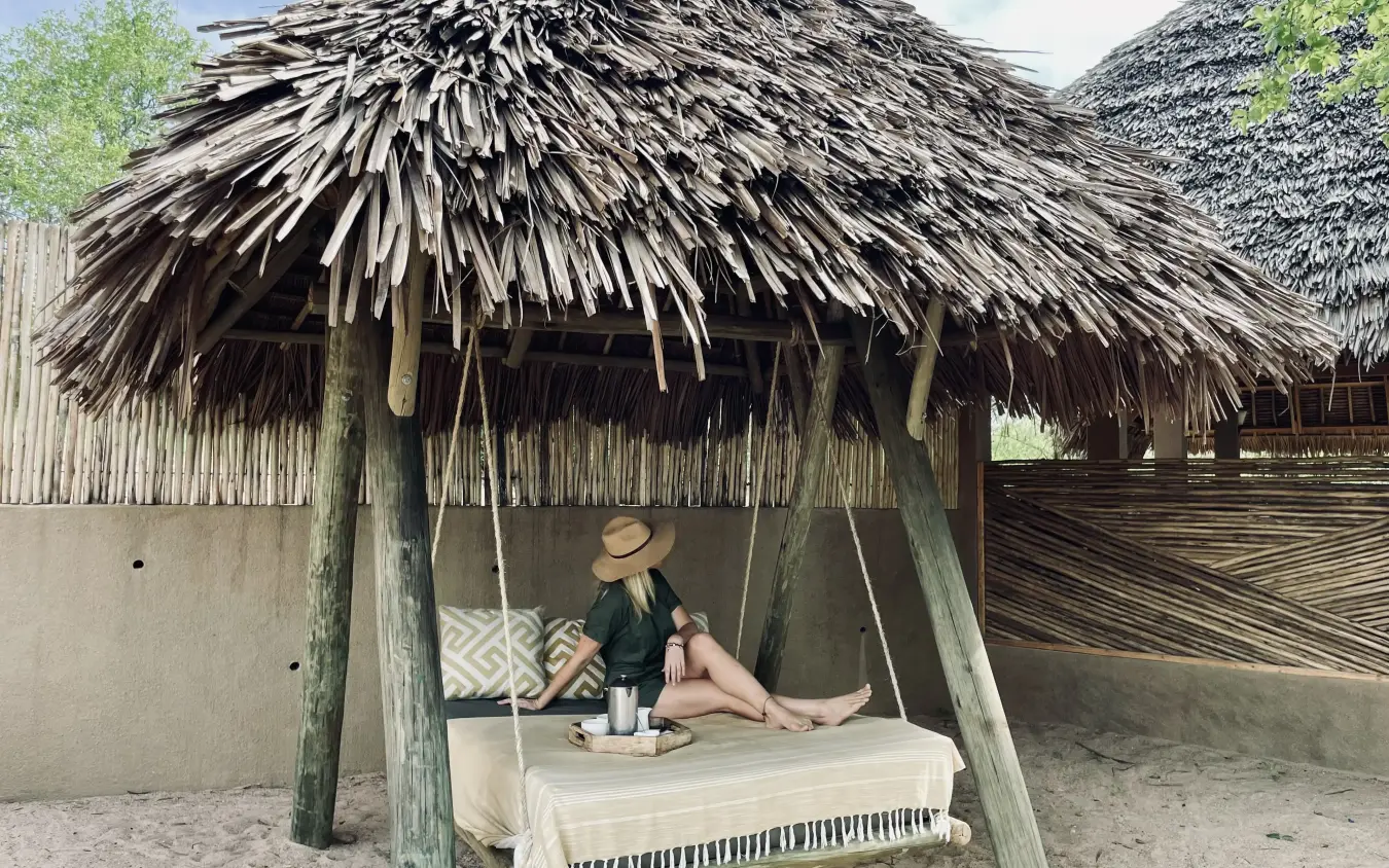 Woman relaxing on bed in thatched-roof beachside cabin, Kichaka Expeditions, Ruaha National Park, Tanzania