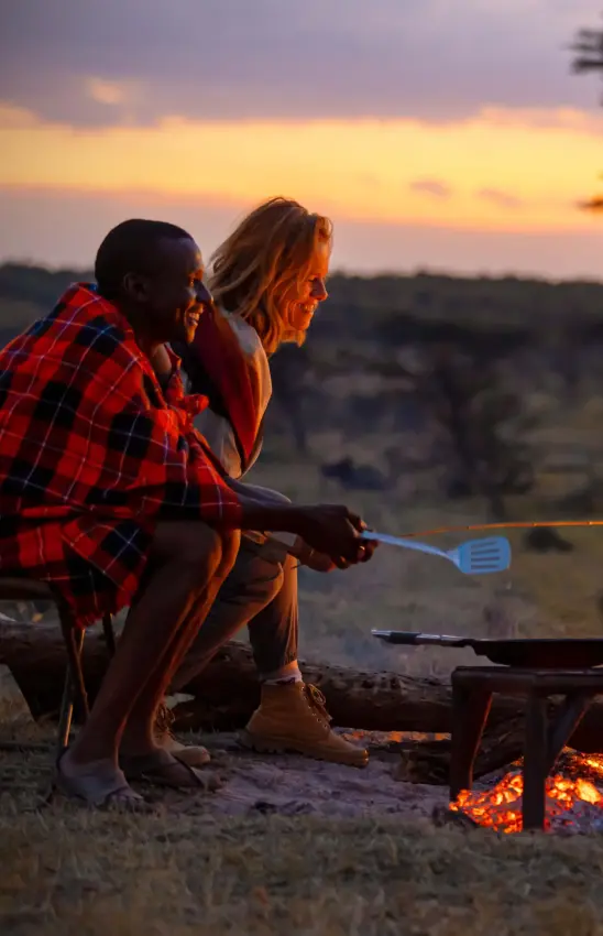 Guests cooking and dining around campfire at sunset, Kicheche Bush Olare, Maasai Mara, Kenya