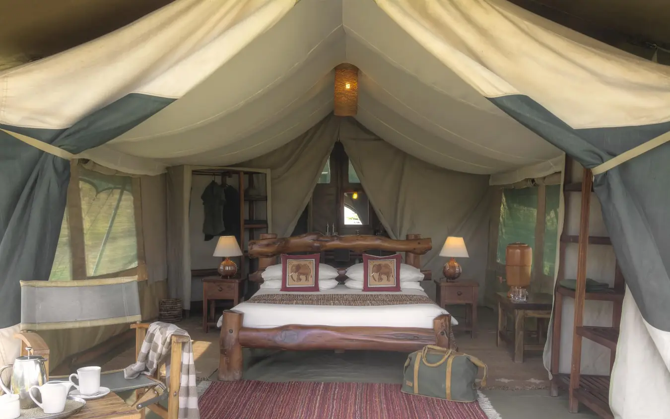 Luxury safari tent bedroom with wooden bed and canvas interior, Kicheche Mara North, Maasai Mara, Kenya