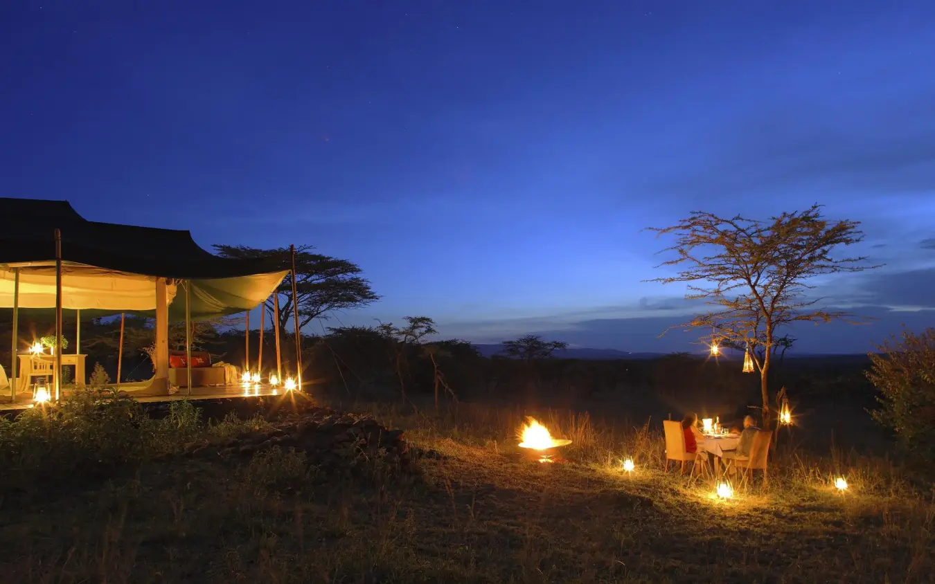 Illuminated safari lodge at dusk with acacia trees, Kicheche Valley Naboisho, Maasai Mara, Kenya