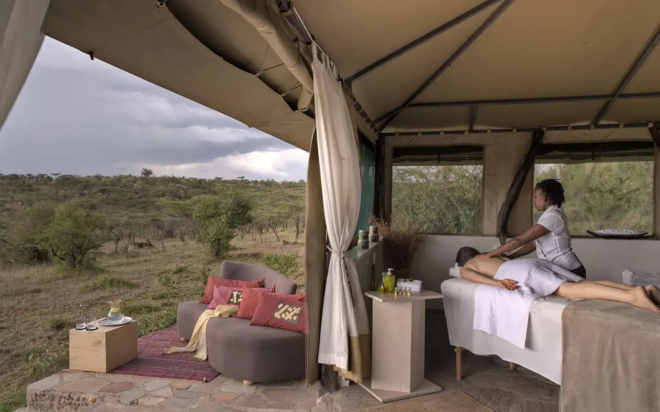 Guest relaxing on bed in safari tent with savanna view, Kicheche Valley Naboisho, Maasai Mara, Kenya