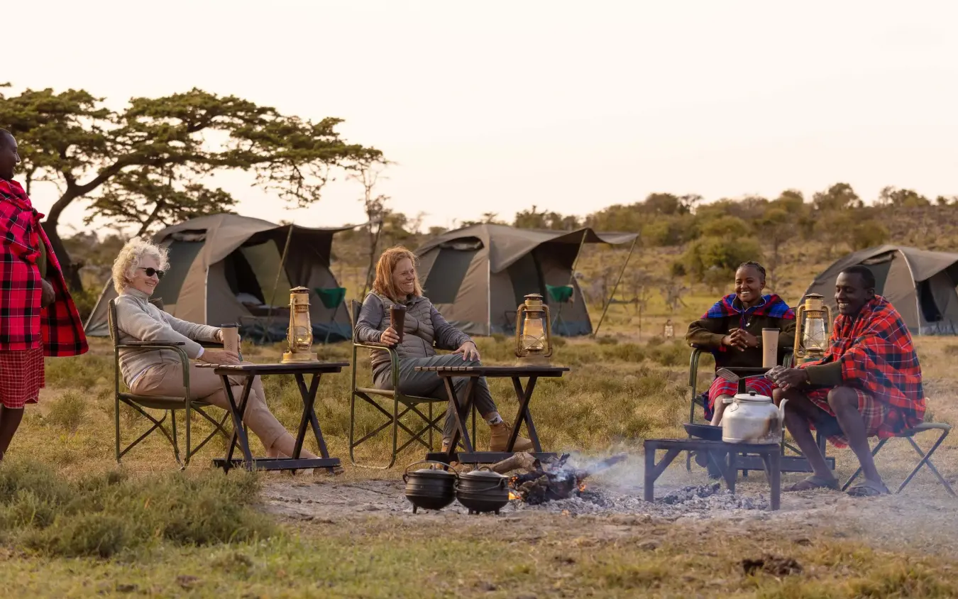 Guests gathered around campfire at safari camp at dusk, Kicheche Valley Naboisho, Maasai Mara, Kenya