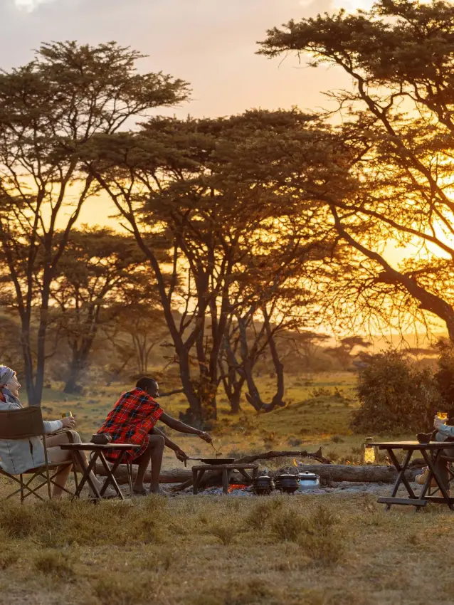 Guests dining outdoors at sunset under acacia trees, Kicheche Valley Naboisho, Maasai Mara, Kenya