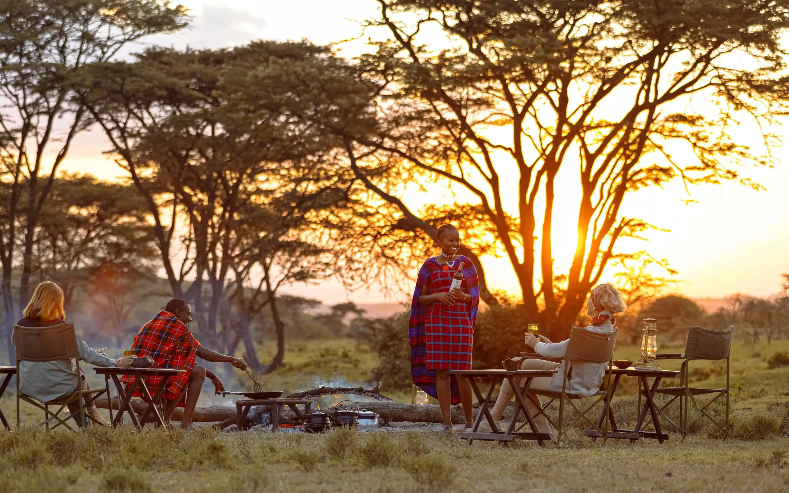 Guests gathered around campfire at sunset in savanna, Kicheche Valley Naboisho, Maasai Mara, Kenya