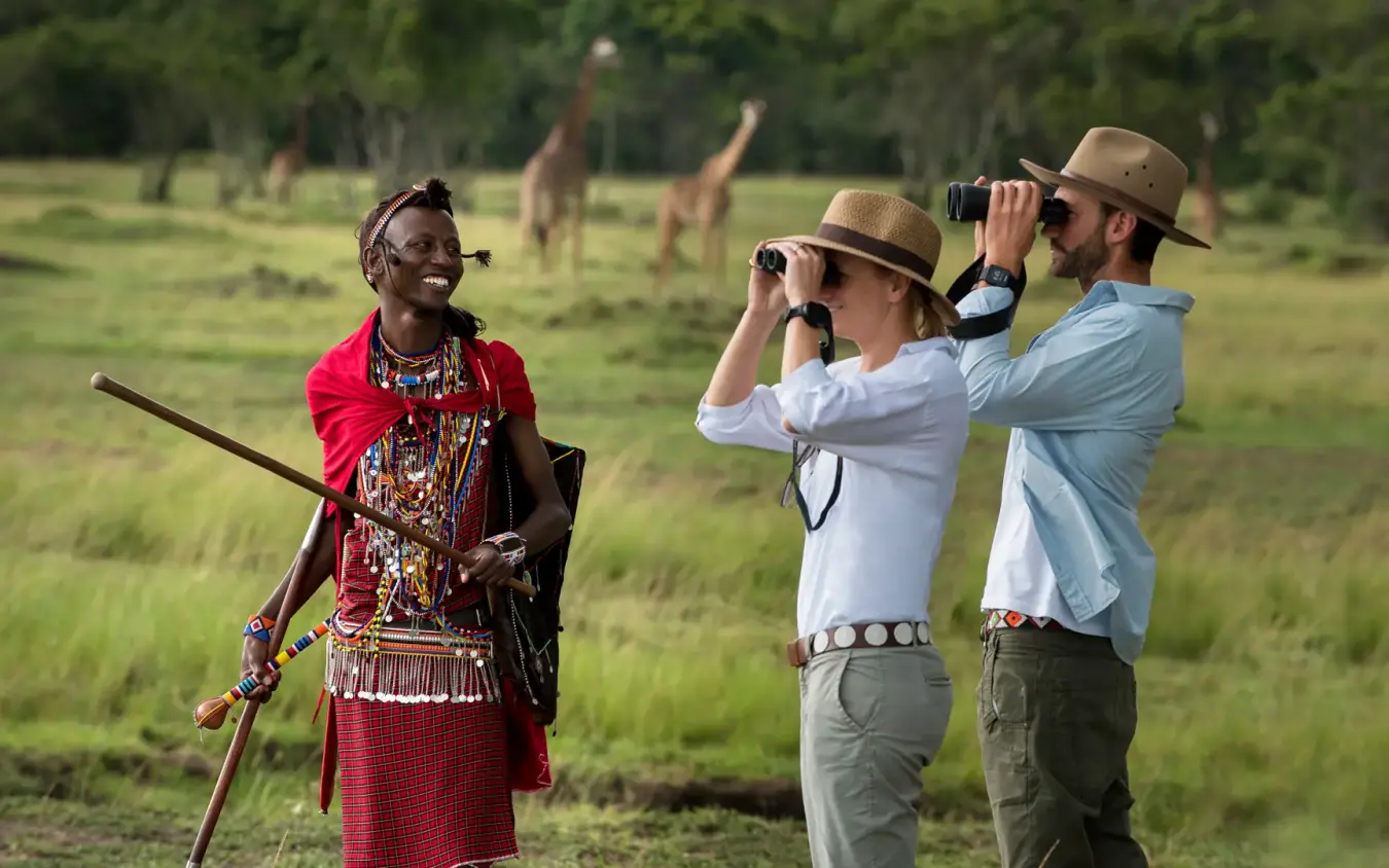 Local guide with tourists using binoculars for wildlife viewing in grassland, Kichwa Tembo Tented Camp, Maasai Mara, Kenya