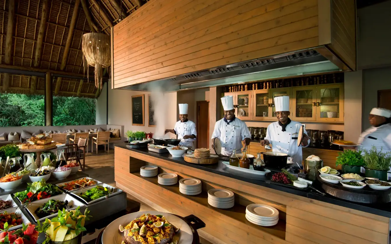 Open-plan lodge kitchen with chefs preparing meal for dining guests, Kichwa Tembo Tented Camp, Maasai Mara, Kenya