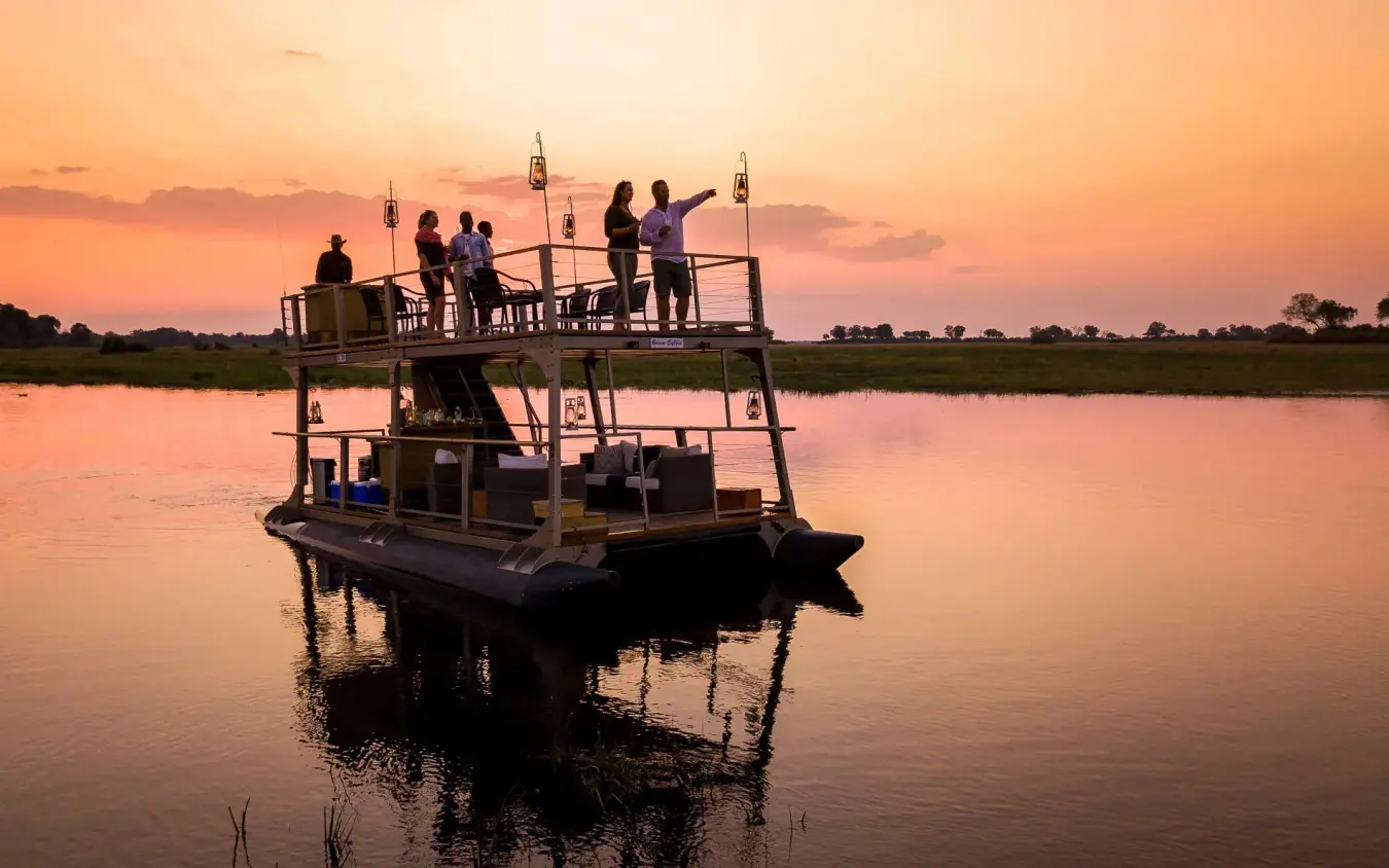 Guests on boat deck at sunset over water, King’s Pool, Linyanti Wildlife Reserve, Botswana