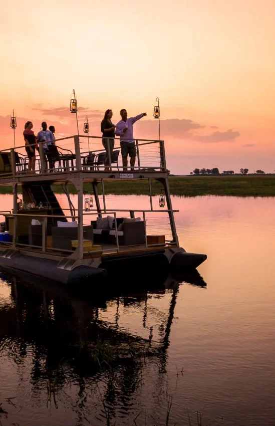 Guests on boat deck at sunset over water, King’s Pool, Linyanti Wildlife Reserve, Botswana