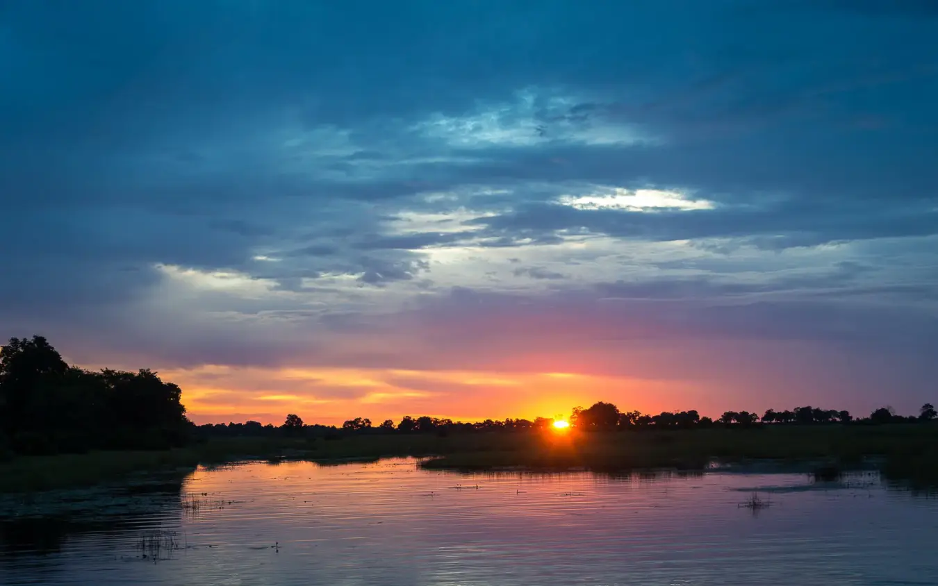 Sunset over river with silhouetted trees and wildlife, King’s Pool, Linyanti Wildlife Reserve, Botswana