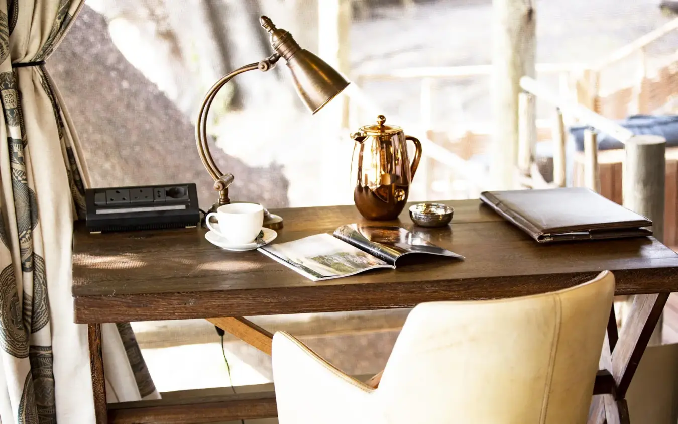 Wooden desk with lamp, coffee cup, and notebooks, King’s Pool, Linyanti Wildlife Reserve, Botswana