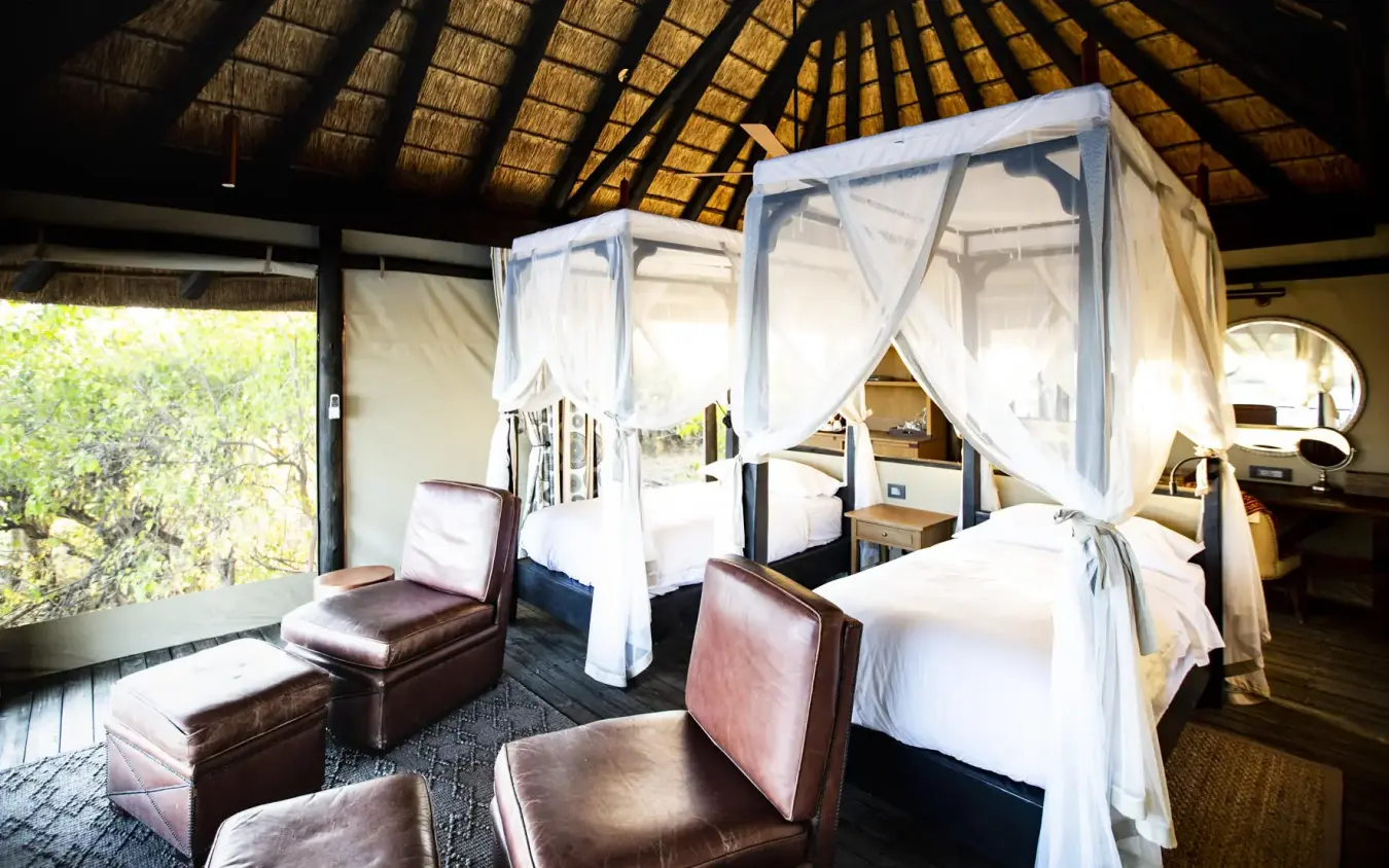 Spacious bedroom with white four-poster canopy bed and leather seating, King’s Pool, Linyanti Wildlife Reserve, Botswana