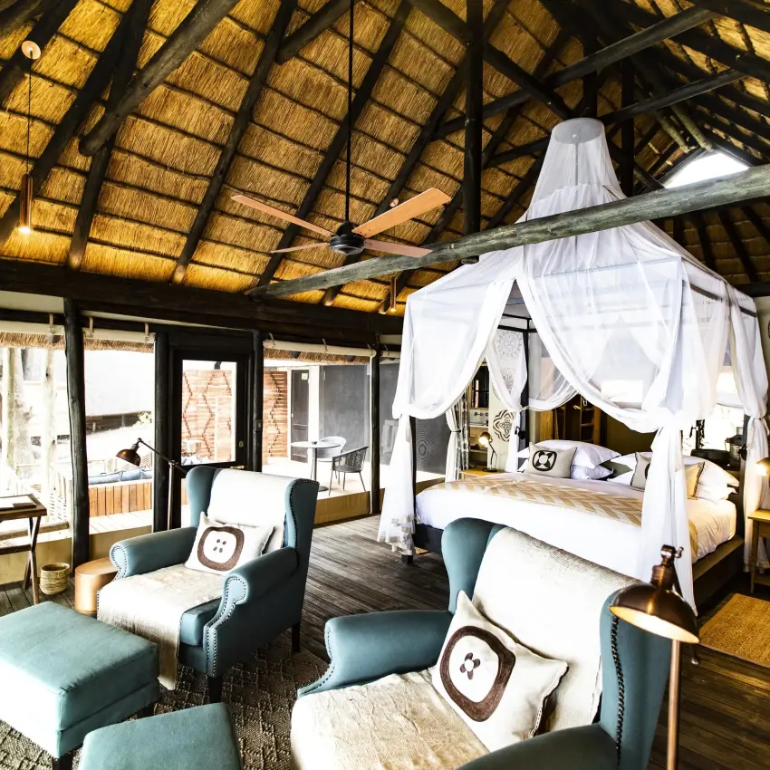 Spacious bedroom with canopy bed and seating area under thatched roof, King’s Pool, Linyanti Wildlife Reserve, Botswana