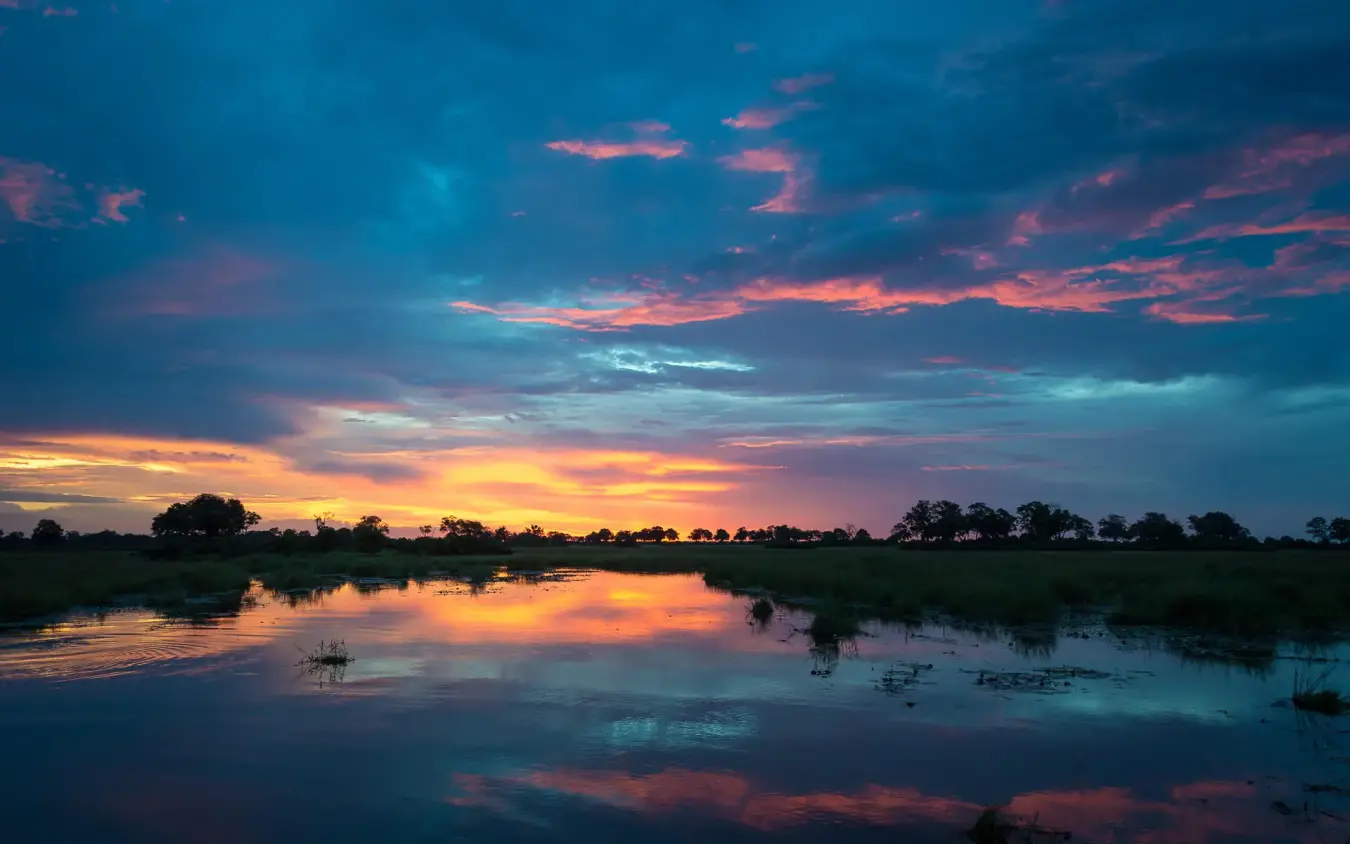 Sunset reflected in still water with trees silhouetted, King’s Pool, Linyanti Wildlife Reserve, Botswana