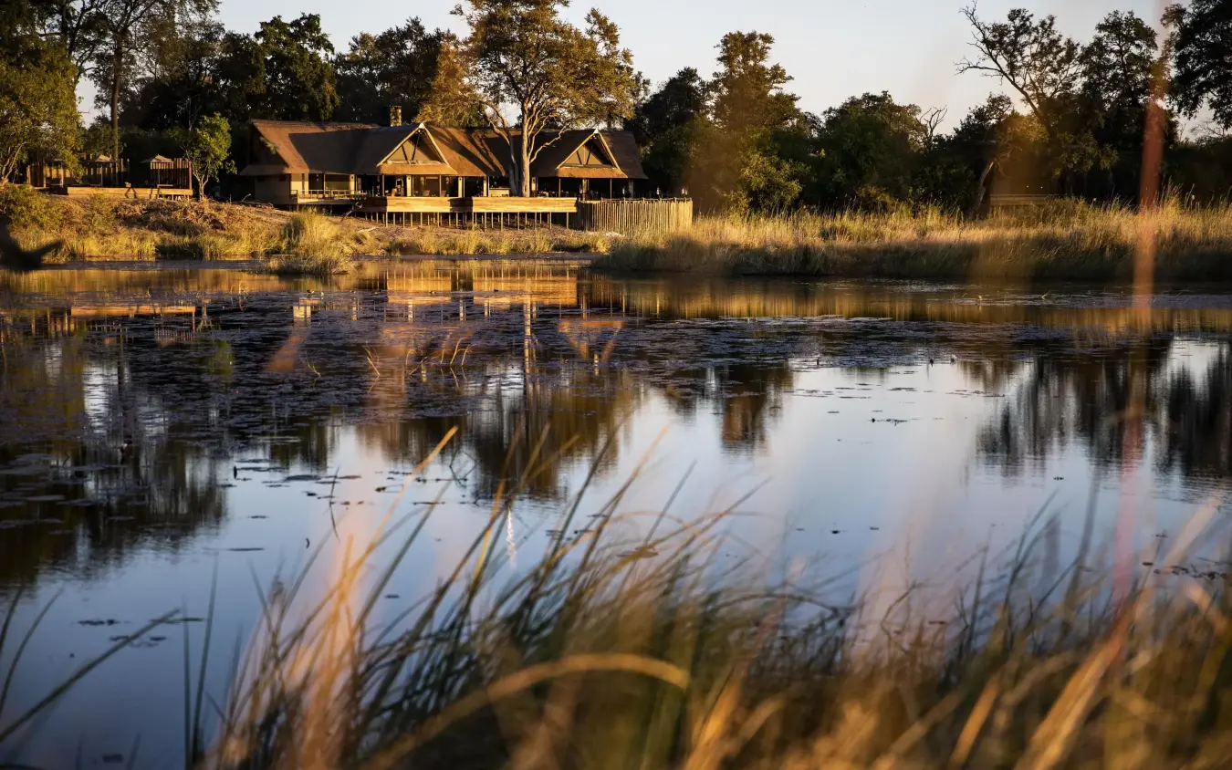 Waterfront lodge at golden hour with reflection in still water, King’s Pool, Linyanti Wildlife Reserve, Botswana