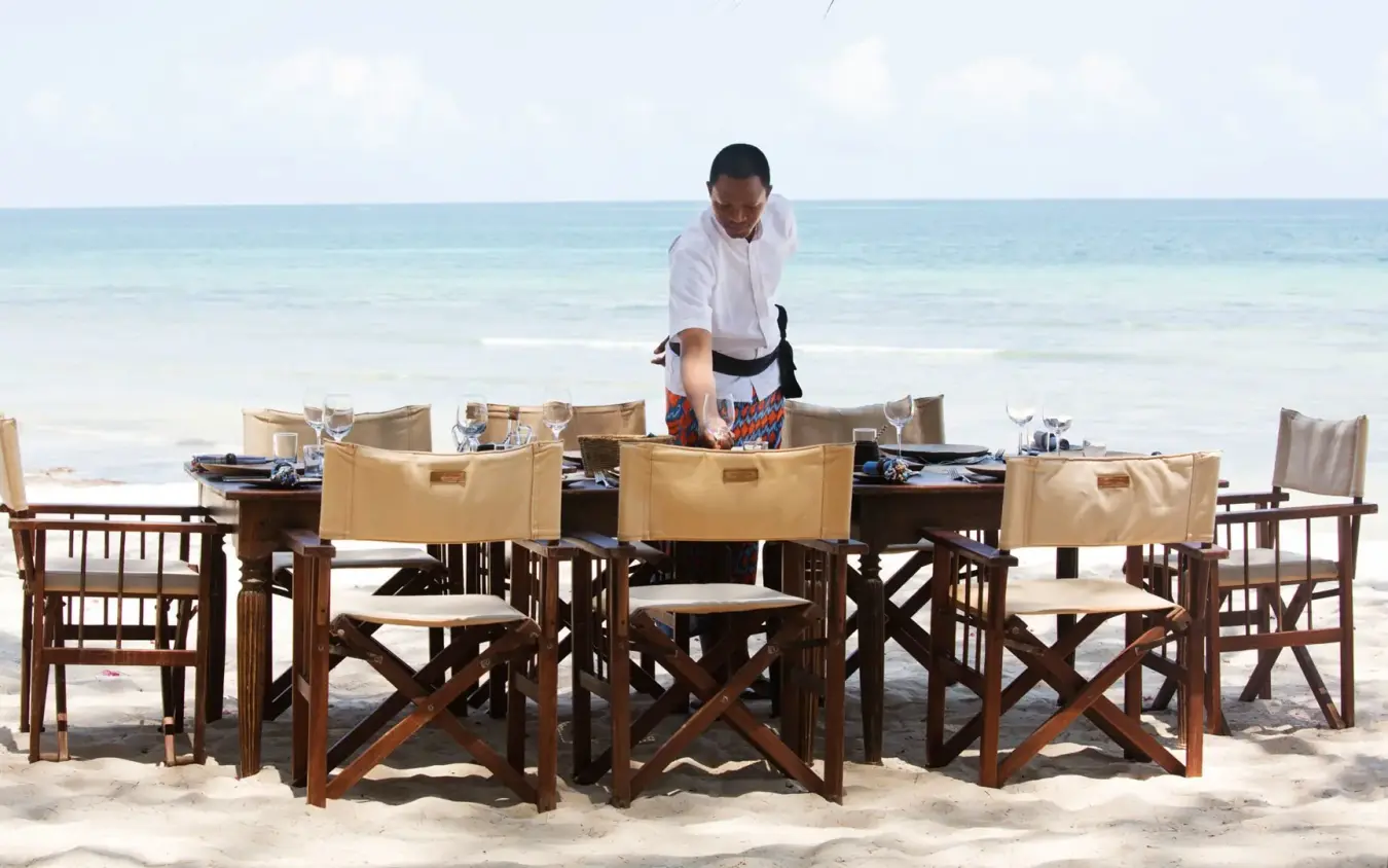 Server setting up beachfront dining table on sand with ocean view, Kinondo Kwetu, Diani Beach, Kenya