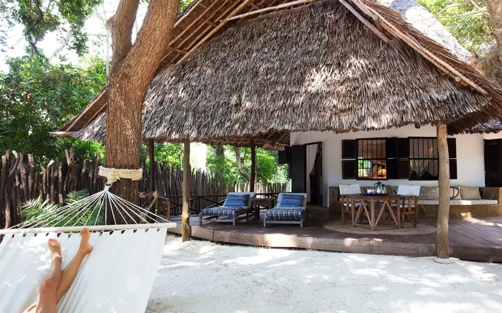 Thatched roof beach lodge with hammock and shaded veranda under large trees, Kinondo Kwetu, Diani Beach, Kenya