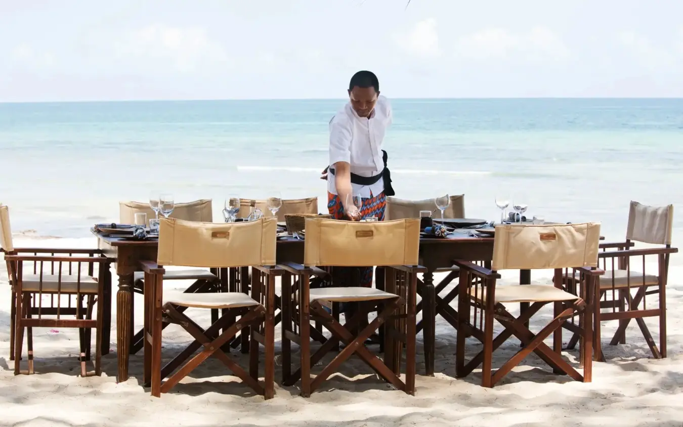 Server setting outdoor dining table on beach at ocean's edge, Kinondo Kwetu, Diani Beach, Kenya