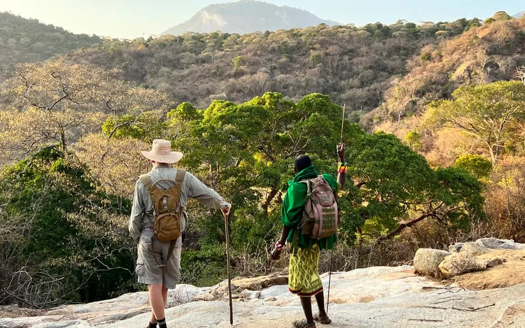 Two hikers walking on rocky outcrop overlooking forested valley, Kenya