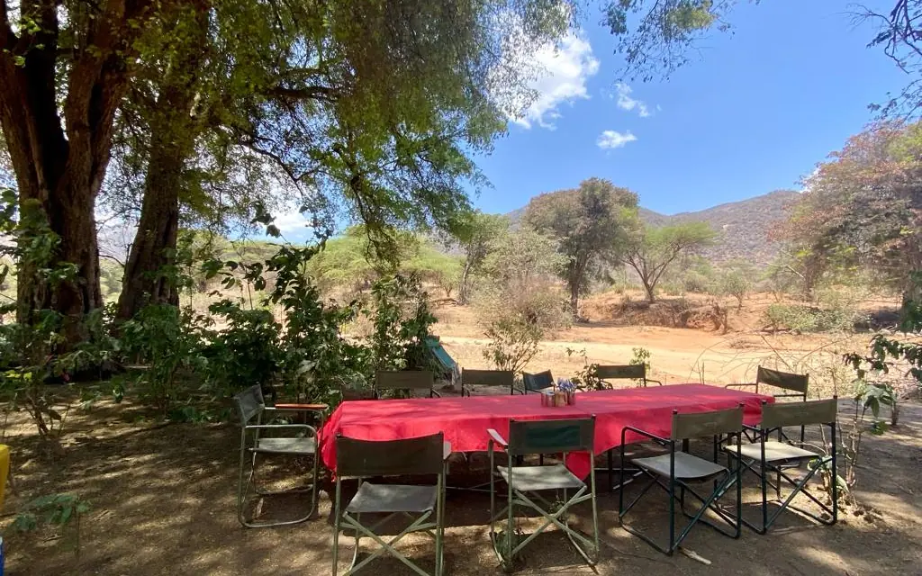 Red tablecloth dining setup under large shaded tree, Kitich Camp, Northern Kenya, Kenya