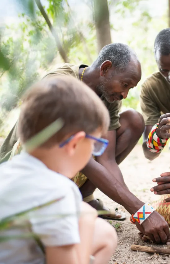 Group learning fire-making skills in forest setting, Kitich Camp, Northern Kenya, Kenya