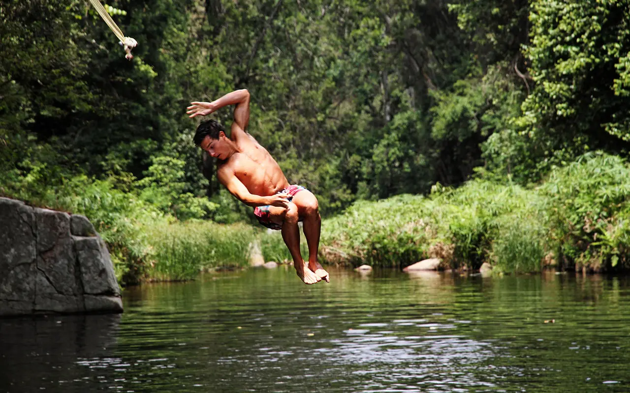 Guest swinging on rope over river in forest, Kitich Camp, Northern Kenya, Kenya